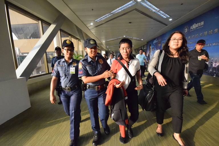 Maria Ressa, ao centro, é escoltada por policiais após desembarcar na capital Manila nesta sexta (29)