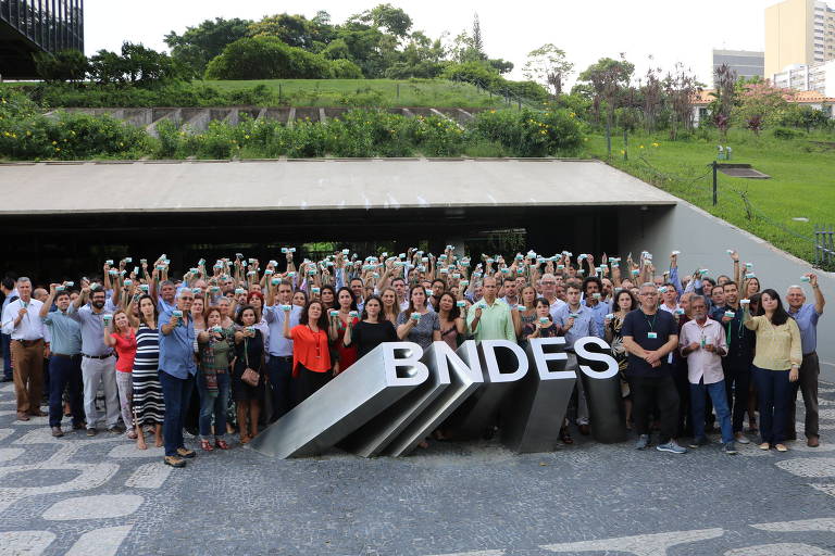 Cerca de uma centena de funcionários do BNDES se manifestam em apoio aos empregados denunciados pelo Ministério Público, no Rio, segurando os crachás em frente ao letreiro do prédio