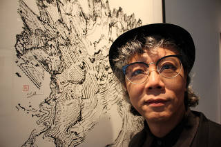 Hong Kong artist Victor Wong stands next to an artwork from his exhibition 'Far Side of the Moon' at 3812 Gallery in London