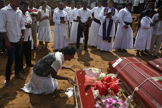 A woman reacts next to a coffin during a mass burial of victims at a cemetery near St. Sebastian Church in Negombo