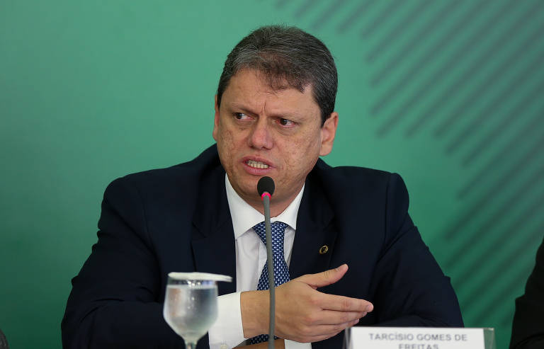 O ministro da Infraestrutura, Tarcísio Freitas, aparece sentado, na frente de um fundo verde, concedendo uma entrevista. 