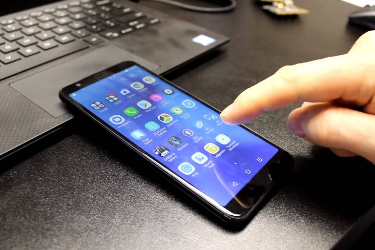Mão aponta para celular, como se fosse apertar em aplicativo.