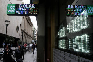 Pedestrians walk past an electronic board displaying currency rates in Buenos Aires' financial district