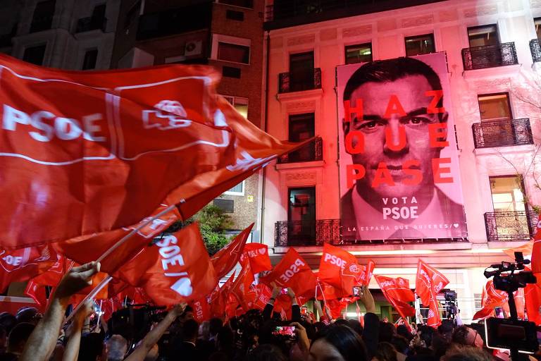 Apoiadores do PSOE comemoram em frente a sede do partido em Madri, que tem na fachada cartaz com o rosto de Pedro Sánchez 