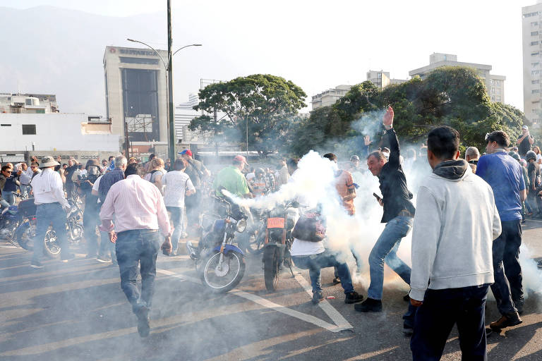 Manifestantes tentam se proteger de disparo de bomba de gás lacrimogêneo em frente à base aérea de La Carlota