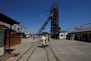 FILE PHOTO: Mine workers walk past the pit head at Sibanye Gold's Masimthembe shaft in Westonaria