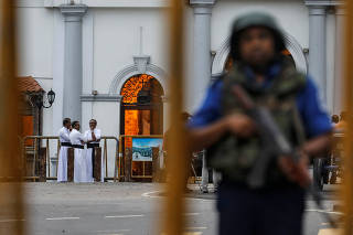 Priests are seen in the background as a security personnel stands guard in front of St Anthony's Shrine, days after a string of suicide bomb attacks across the island on Easter Sunday, in Colombo