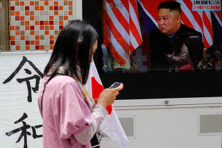 A woman walks past a television screen showing North Korea's leader Kim Jong Un during a news report on North Korea firing several short-range projectiles from its east coast, in Tokyo