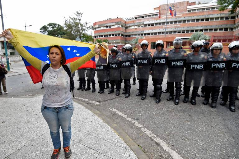 Manifestante exibe bandeira venezuelana na frente de agentes de segurança ao lado do comando da Marinha em Caracas 