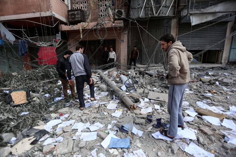 Palestinos observam prédio destruído por ataque israelense na cidade de Rafah, na faixa de Gaza 