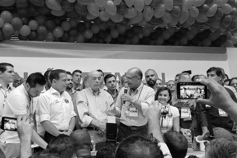 No centro, o presidente nacional do PSDB, Geraldo Alckmin, fala ao microfone em convenção estadual do partido, em São Paulo; próximos a ele estão o senador José Serra e o governador João Doria