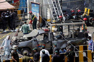 Police officers survey while rescue workers attend to a body at the site of a blast in Lahore, Pakistan