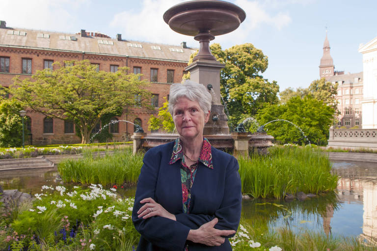 A pedagoga, uma senhora de cabelos brancos, em frente a uma fonte num jardim
