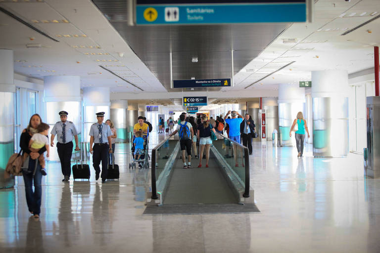 Foto mostra alguns passageiros na esteira rolantes, no aeroporto de Viracopos. Ao redor, há algumas pessoas andando pelos corredores, que são brancos e iluminados.