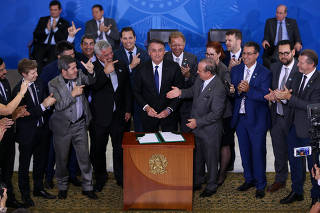 Parlamentares fazem o símbolo da arma com os dedos ao lado de Bolsonaro