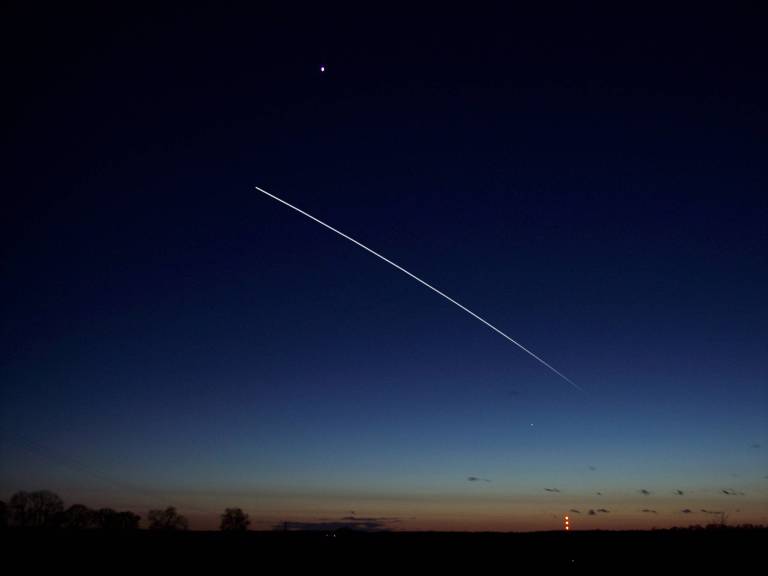 Céu esrelado sobre cidade com um longo traço representando a trajetória da ISS