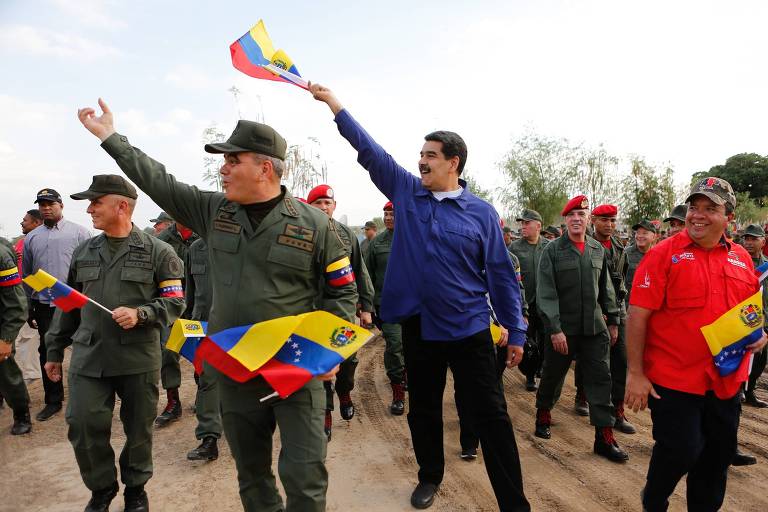 Foto divulgada pelo Palácio de Miraflores mostra o ditador da Venezuela, Nicolás Maduro (de azul), ao lado do ministro da Defesa, Vladimir Padrino (esq.) com bandeiras do país acenando para militares no estado de Aragua