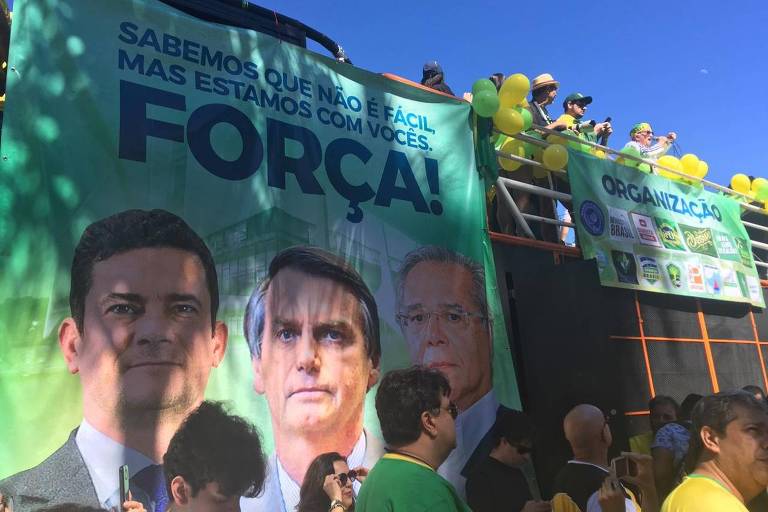 Carro de som com faixa grande com rostos de Moro, Guedes e Bolsonaro, e a frase "Sabemos que não é fácil, mas estamos com vocês. Força!"