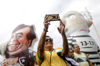 A woman takes a selfie between inflatable dolls, depicting former Brazilian president Luiz Inacio Lula da Silva and Lower House President Rodrigo Maia during a pro-government demonstration in Rio de Janeiro
