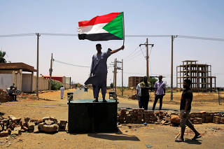 A Sudanese protester holds a national flag as he stands on a barricade along a street, demanding that the country's Transitional Military Council hand over power to civilians, in Khartoum