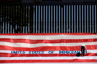 Roberto Marquez, known as Roberz, writes on a large U.S. flag as part of a protest called 'United States of Immigrants', aimed to demand respect for the migrants, near a border wall in El Paso, Texas, as pictured from Ciudad Juarez