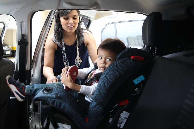 Mulher ajusta cadeirinha com criança dentro de um carro.