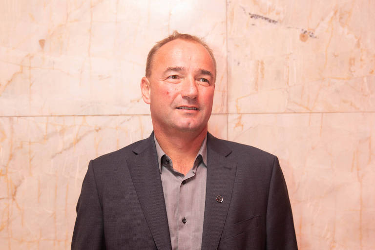 Retrato do executivo usando terno e camisa sem gravata, em frente a parede de mármore