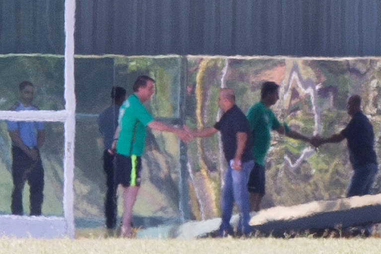 Jair Bolsonaro, vestido com camiseta e berbuda, cumprimentando o deputado Major Vitor Hugo