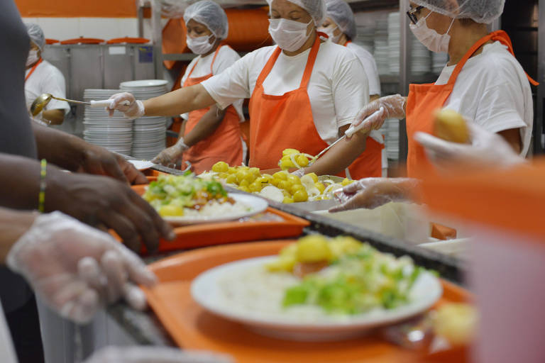 Restaurante Bom Prato do bairro de Campos Elíseos, na região central de São Paulo. Na foto, pessoas se servem em bandejas laranjas e funcionários uniformizados colocam a comida no prato.