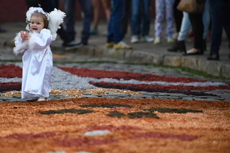 Criança vestida de anjo, à esquerda, passeia sobre tapete de Corpus Christi