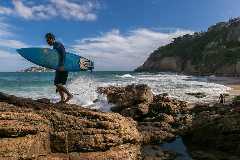 Surfista caminha pelas pedras que dão acesso à praia da Joatinga, escondida nas encostas do morro do Joá, no meio do caminho entre as zonas sul e oeste do Rio de Janeiro