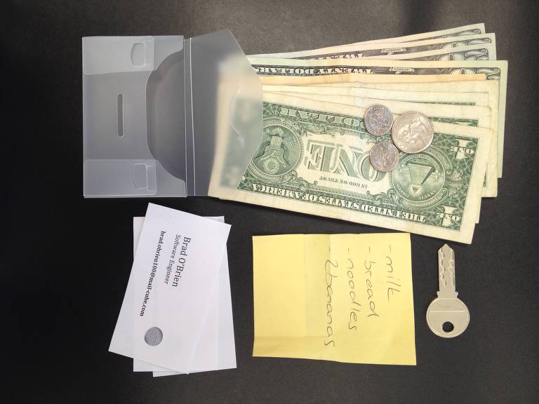 Carteira de plático transparente, notas de dólar, lista de compras, cartão de visitas e chave, em fundo preto