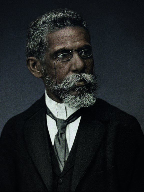 a imagem colorizada mostra Machado de Assis, homem negro de pele retinta, que usa barba e cabelos grisalhos