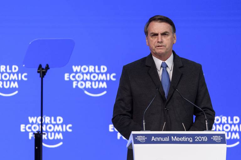 O presidente Jair Bolsonaro discursa no Fórum Econômico Mundial de 2019. Atrás dele, um painel azul em que aparecem quatro inscrições "World Economic Forum"