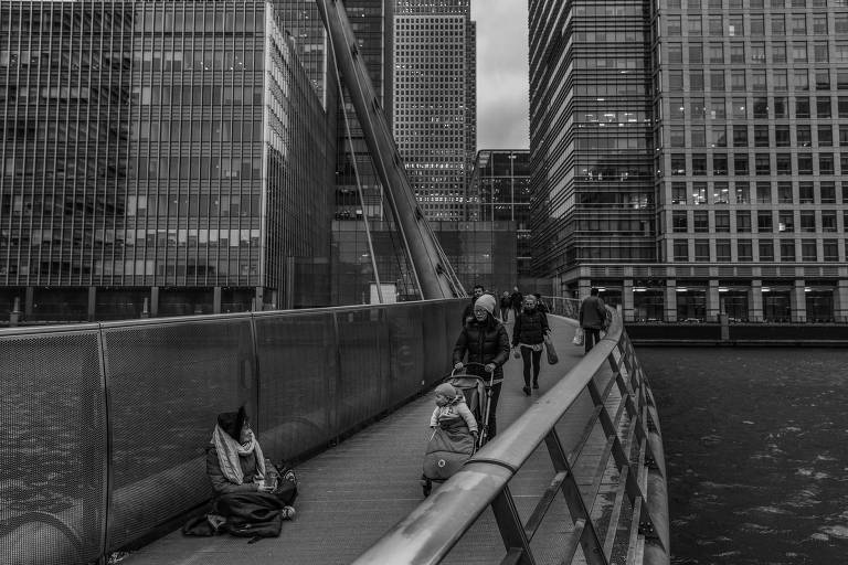 Mulher pede esmola em ponte para pedestres de Canary Wharf, em Londres