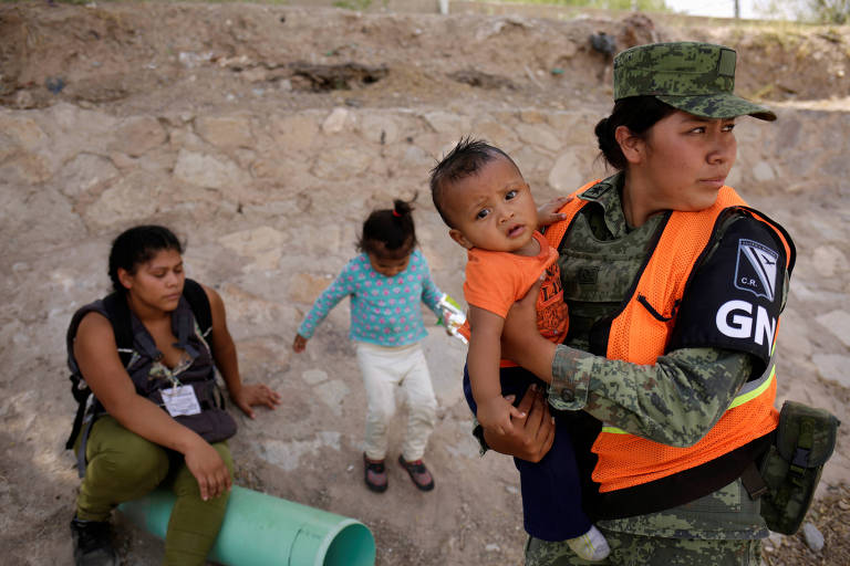 Membro da Guarda Nacional do México segura um bebê hondurenho após impedir que el e sua mãe cruzassem a fronteira entre Ciudad Juarez e El Paso, no Texas