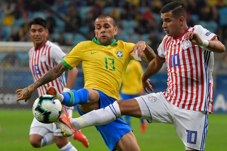 Daniel Alves divide bola com Derliz González na partida entre Brasil e Paraguai na quinta-feira (27)