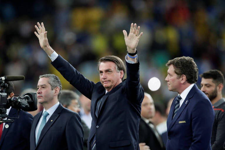 Jair Bolsonaro acena para a torcida ao lado de Rogério Caboclo, presidente da CBF, e Alejandro Domínguez, presidente da Conmebol, na final da Copa América de 2019, disputada no Brasil