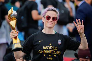 Megan Rapinoe gestures the number 4 with her fingers as she holds the Trophy for the FIFA Women's World Cup while the U.S. team arrives at the Newark International Airport, in Newark