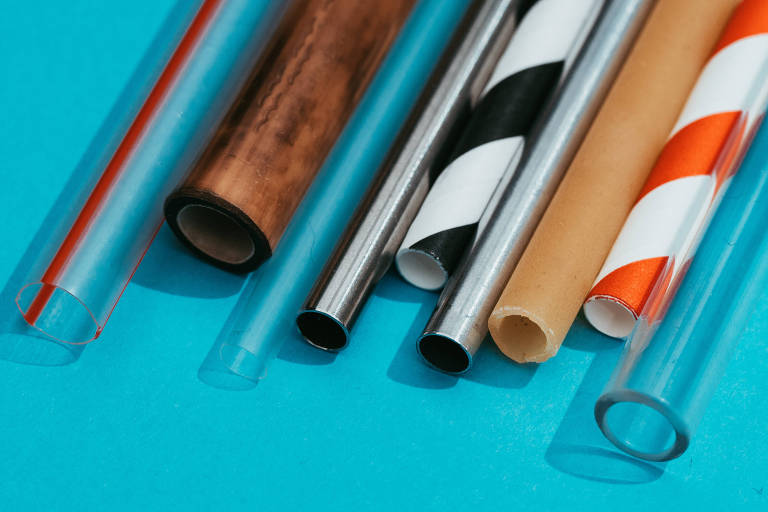 Canudos de vidro, metal, bambu, madeira e plástico lado a lado sob um fundo azul