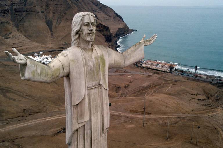 estátua de um Cristo em cima de uma colina; ao fundo, o mar