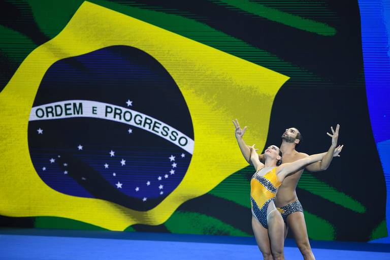 Atletas em frente à bandeira do Brasil