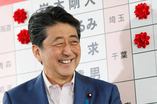 Japan's Prime Minister Shinzo Abe, who is also leader of the ruling Liberal Democratic Party (LDP), reacts as he puts a rosette on the name of a candidate who is expected to win the upper house election, at the LDP headquarters in Tokyo