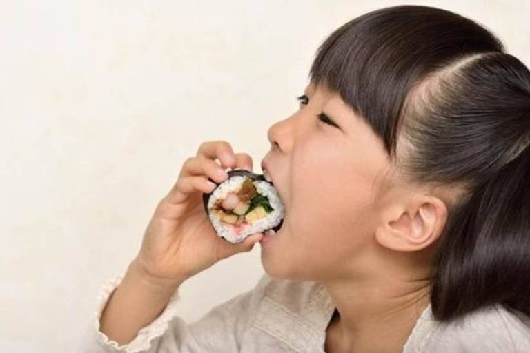 Garota oriental comendo um sushi