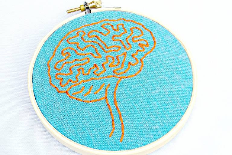 Na foto, há um tecido azul com um cérebro bordado em laranja