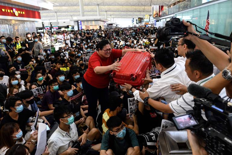 Turista tenta passar sua mala ao tentar entrar no aeroporto de Hong Kong, bloqueado nesta terça (13)