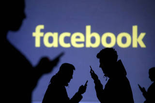 FILE PHOTO: Silhouettes of mobile users are seen next to a screen projection of the Facebook logo in this picture illustration