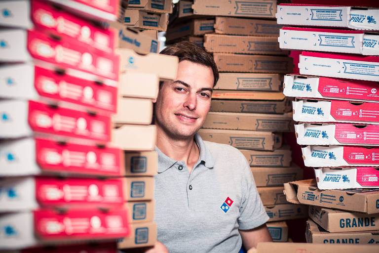 Marcelo Romi está sentado entre pilhas de caixas de pizza