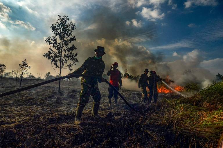 Oficiais da força-tarefa de incêndios florestais e terrestres tentam apagar um incêndio com canos de água em uma plantação de óleo de palma em Pekanbaru, na província de Riau, 
