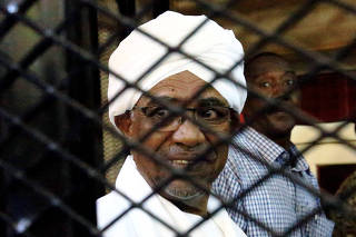 Sudan's former president Omar Hassan al-Bashir smiles as he is seen inside a cage at the courthouse where he is facing corruption charges, in Khartoum
